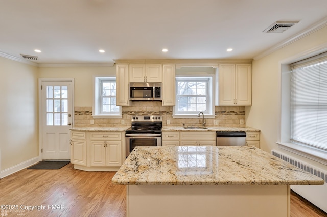 kitchen with stainless steel appliances, radiator heating unit, a sink, plenty of natural light, and ornamental molding