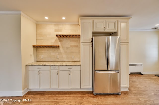 kitchen featuring freestanding refrigerator, radiator heating unit, backsplash, light stone countertops, and light wood-style floors