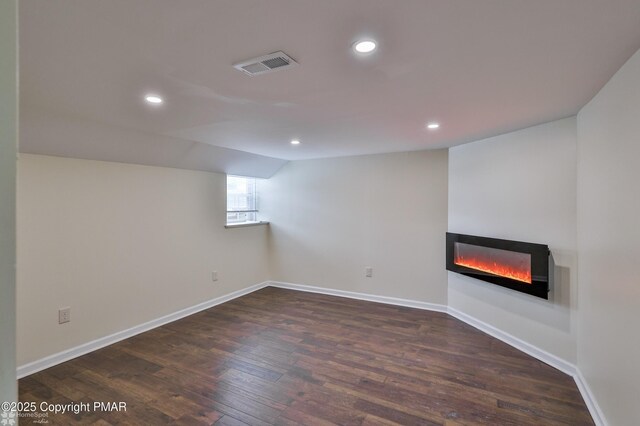 below grade area featuring a glass covered fireplace, dark wood-style flooring, recessed lighting, and baseboards