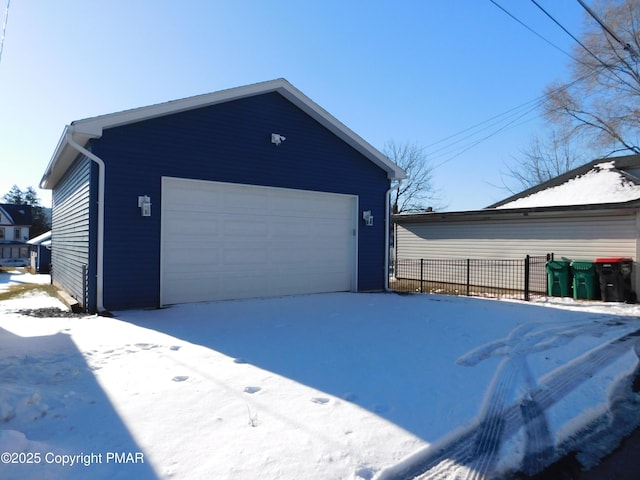 snow covered garage with a detached garage and fence