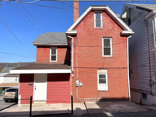 view of front facade featuring brick siding, roof with shingles, and a chimney