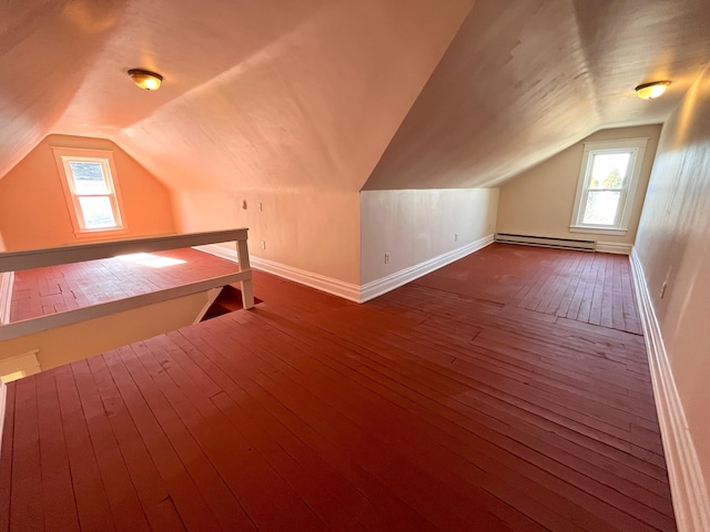 additional living space with a baseboard heating unit, vaulted ceiling, a healthy amount of sunlight, and dark wood-style flooring