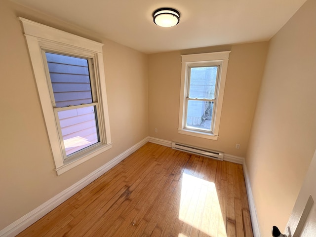 empty room featuring baseboard heating, baseboards, and hardwood / wood-style floors