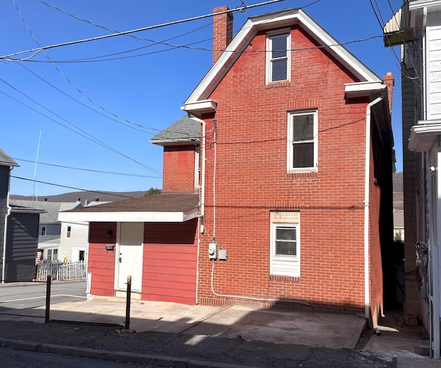 exterior space featuring brick siding, a chimney, and roof with shingles