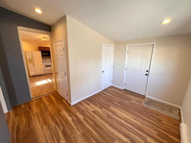 unfurnished bedroom featuring lofted ceiling, wood finished floors, white fridge with ice dispenser, baseboards, and baseboard heating