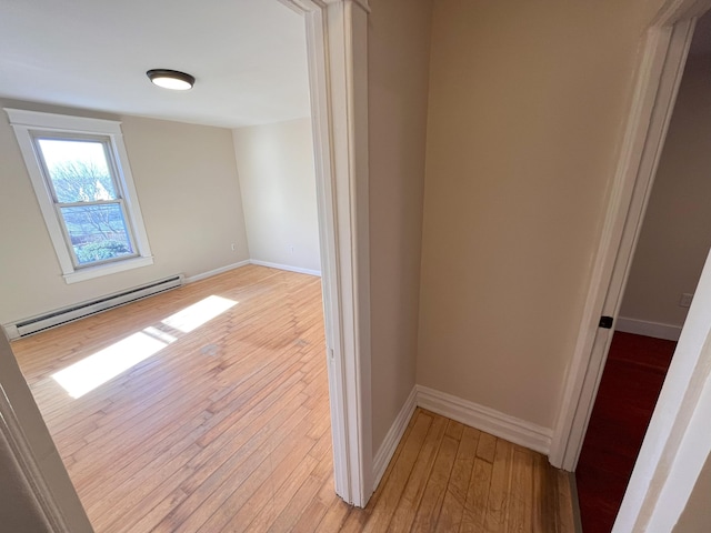 interior space with light wood-type flooring, a baseboard heating unit, and baseboards