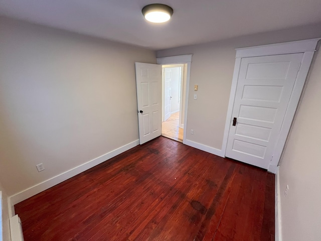 unfurnished bedroom with baseboards and dark wood-style flooring