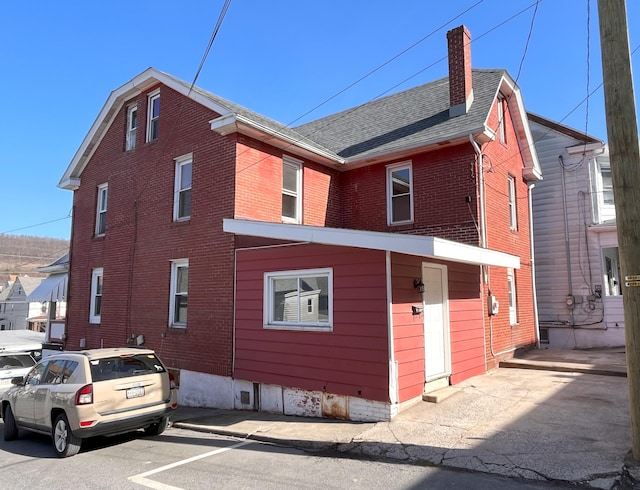 view of home's exterior featuring brick siding, roof with shingles, and a chimney