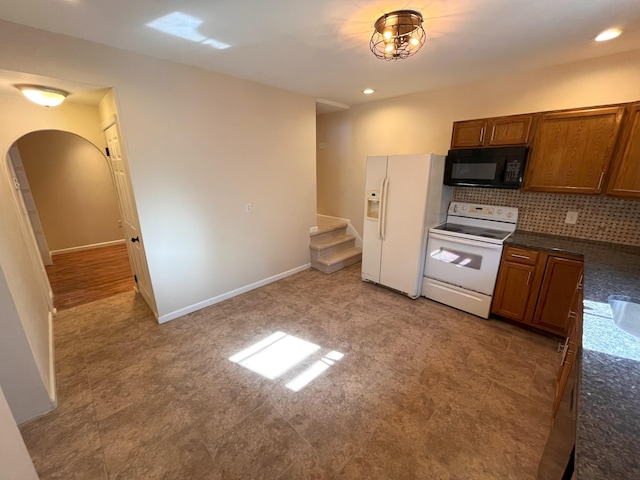 kitchen with white appliances, arched walkways, dark countertops, and brown cabinets