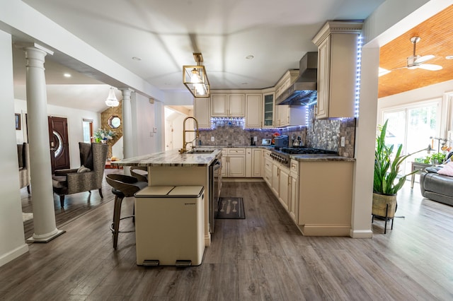 1555 Longleaf Dr, Effort, PA 18330 - kitchen with cream cabinets, wall chimney range hood, stainless steel gas stovetop, decorative columns, and dark wood-style flooring