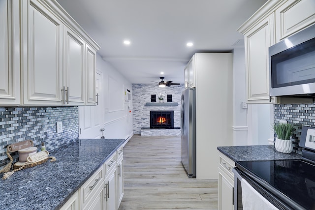3109 Snowden Dr, Bushkill, PA 18324 - kitchen featuring appliances with stainless steel finishes, a fireplace, a ceiling fan, light wood finished floors, and decorative backsplash
