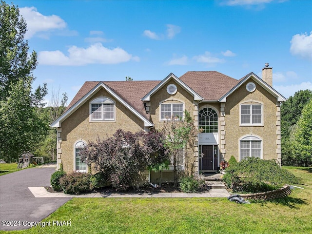 traditional-style home with stucco siding, roof with shingles, a chimney, and a front yard