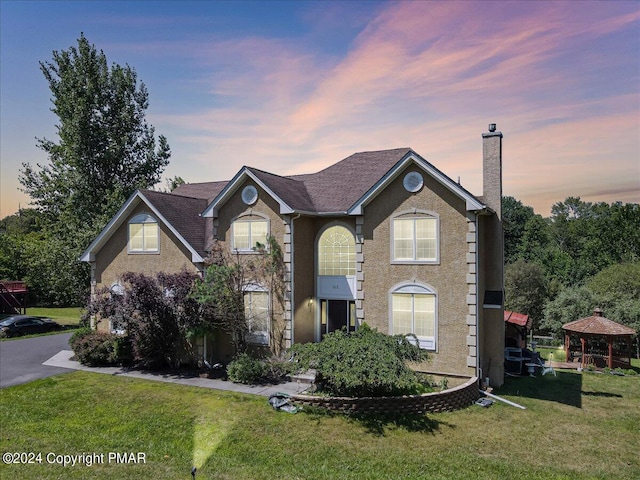 view of front of house featuring a gazebo, stucco siding, a chimney, and a yard