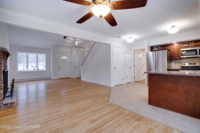 kitchen with appliances with stainless steel finishes, a baseboard radiator, dark stone countertops, decorative backsplash, and light hardwood / wood-style flooring