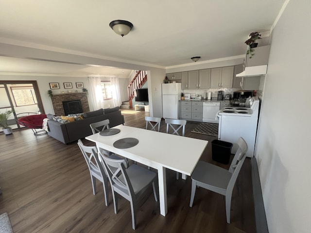 dining space with dark wood-style flooring, crown molding, washer / clothes dryer, stairway, and a brick fireplace