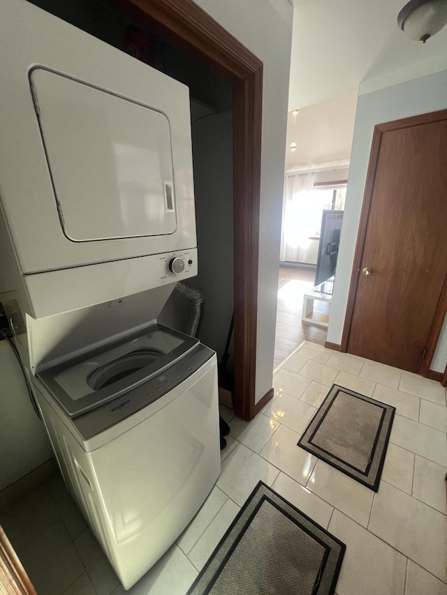 clothes washing area featuring stacked washer and clothes dryer, light tile patterned flooring, baseboards, and laundry area