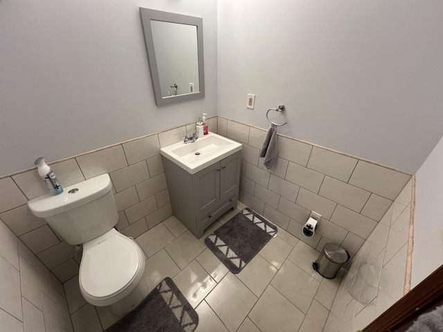 half bath featuring tile patterned flooring, toilet, a wainscoted wall, vanity, and tile walls