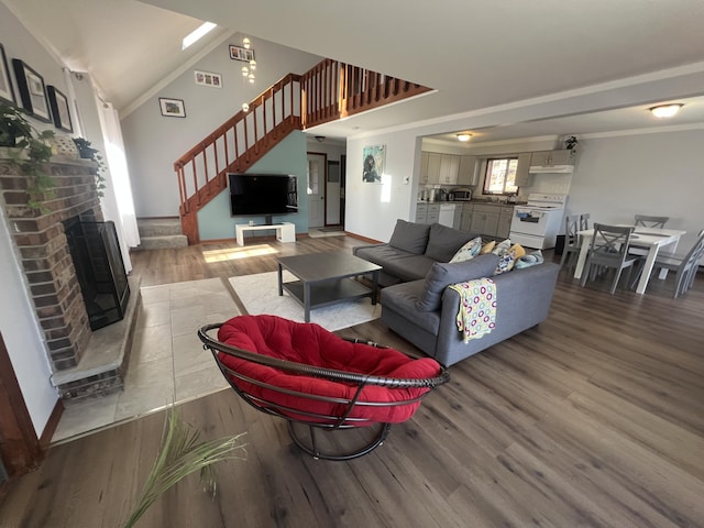 living room featuring a high ceiling, wood finished floors, stairs, a brick fireplace, and crown molding