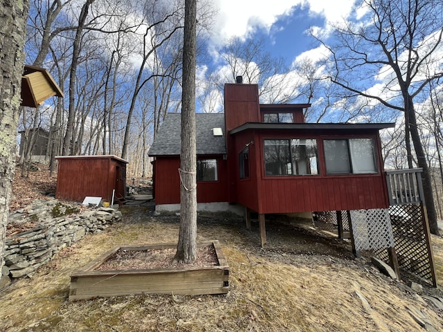 view of side of home featuring a shingled roof, a chimney, and a sunroom