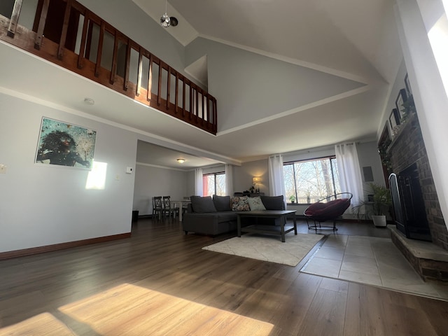 living area with high vaulted ceiling, a brick fireplace, wood finished floors, and baseboards