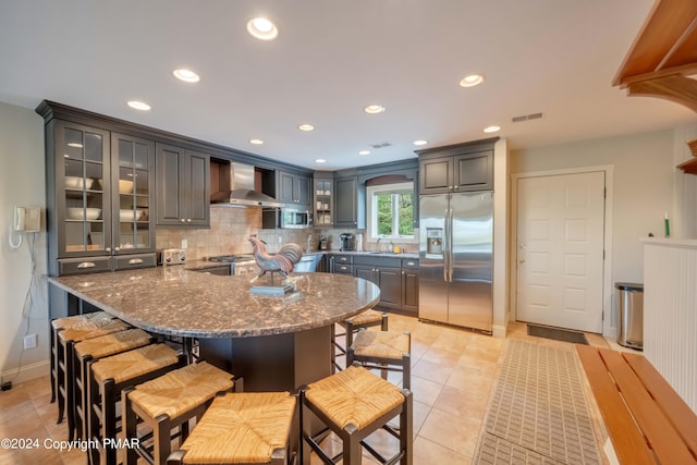 kitchen with stainless steel appliances, visible vents, backsplash, glass insert cabinets, and wall chimney exhaust hood