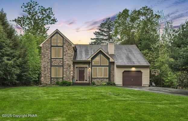 view of front of house featuring an attached garage, a yard, a chimney, stone siding, and aphalt driveway