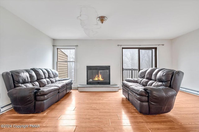 living room with a baseboard heating unit, light wood finished floors, and a glass covered fireplace