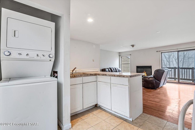 laundry room with laundry area, light tile patterned floors, a glass covered fireplace, stacked washer and clothes dryer, and a sink