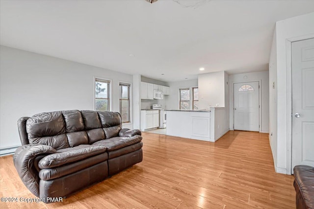 living room with a wealth of natural light, light wood-type flooring, a baseboard heating unit, and baseboards