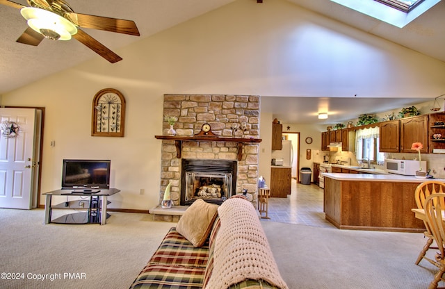 living room featuring a skylight, a fireplace, light carpet, ceiling fan, and high vaulted ceiling