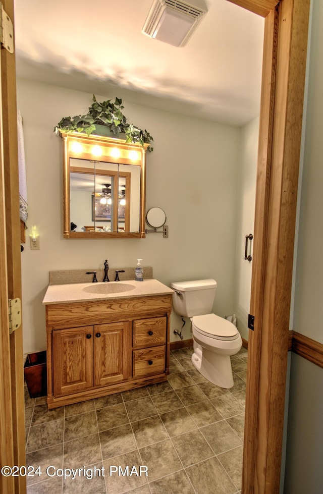 half bathroom with toilet, vanity, visible vents, and baseboards