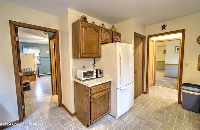 kitchen featuring a toaster, baseboards, light countertops, freestanding refrigerator, and brown cabinets