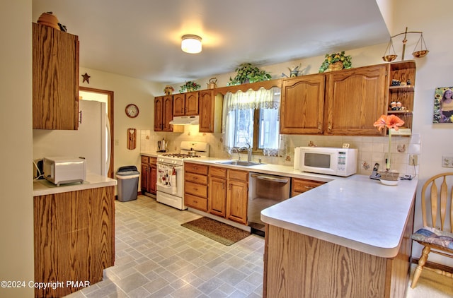 kitchen featuring under cabinet range hood, a peninsula, white appliances, a sink, and decorative backsplash