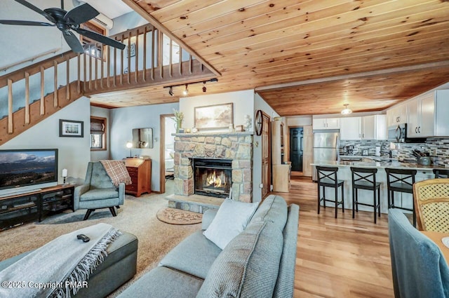 living room featuring light hardwood / wood-style flooring, a fireplace, wooden ceiling, and ceiling fan