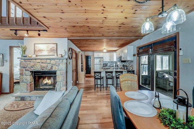 dining area with a fireplace, light hardwood / wood-style floors, rail lighting, and wooden ceiling