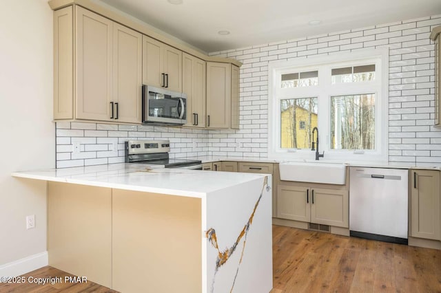 kitchen featuring stainless steel appliances, kitchen peninsula, sink, and decorative backsplash