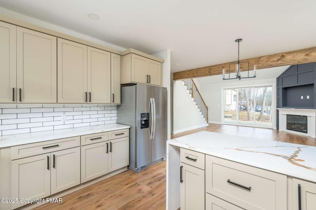 kitchen featuring stainless steel fridge with ice dispenser, hanging light fixtures, beamed ceiling, decorative backsplash, and cream cabinetry