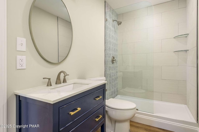 bathroom featuring vanity, hardwood / wood-style floors, toilet, and a tile shower