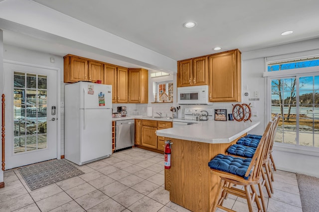 kitchen with white appliances, a kitchen breakfast bar, a peninsula, light countertops, and a sink