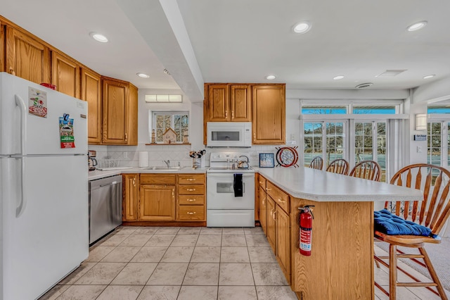 kitchen with a peninsula, white appliances, a breakfast bar, light countertops, and backsplash