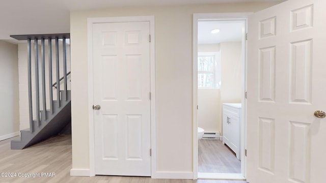 corridor with stairs, baseboard heating, baseboards, and light wood-style floors