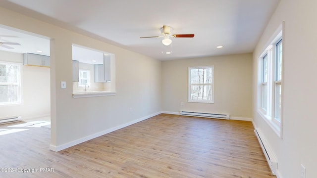 empty room featuring a sink, a ceiling fan, baseboards, light wood-style floors, and baseboard heating