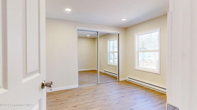 unfurnished bedroom with a baseboard heating unit, recessed lighting, a closet, and wood finished floors