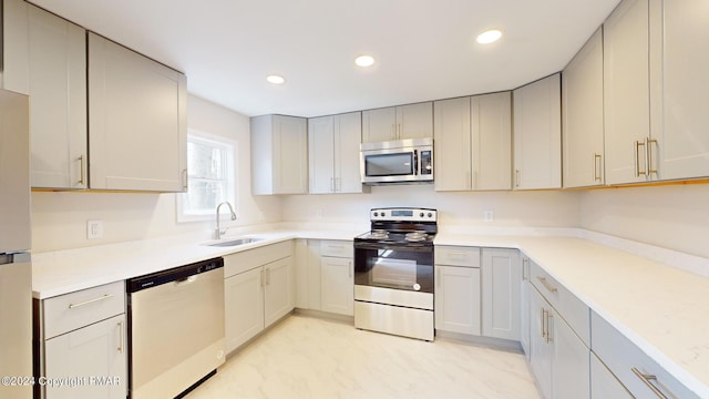 kitchen featuring stainless steel appliances, a sink, light countertops, and recessed lighting