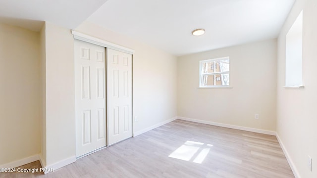 unfurnished bedroom with a closet, baseboards, and light wood finished floors