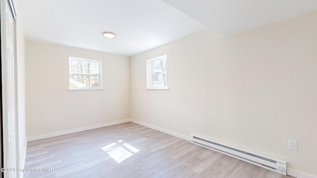 empty room with light wood finished floors, a baseboard radiator, and baseboards