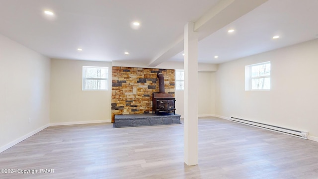 basement with a wealth of natural light, a baseboard radiator, wood finished floors, and a wood stove