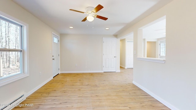 empty room with light wood-type flooring, a baseboard radiator, baseboards, and a wealth of natural light