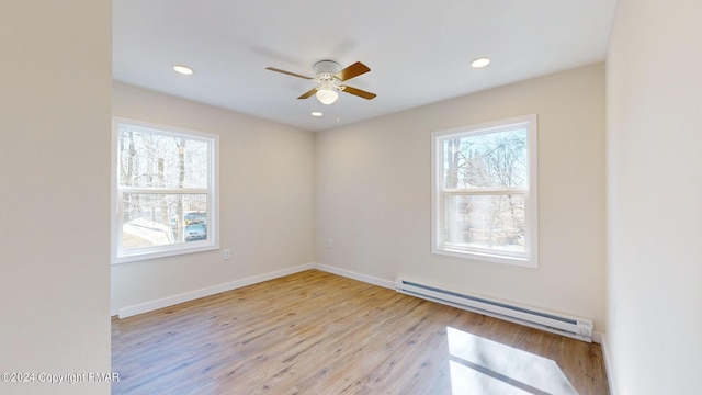 spare room featuring baseboards, light wood-type flooring, a baseboard radiator, and a healthy amount of sunlight