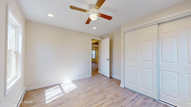 unfurnished bedroom with baseboard heating, light wood-type flooring, a closet, and baseboards